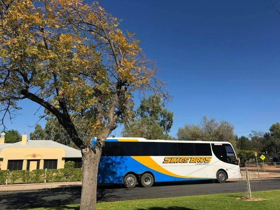 A Blue and Yellow Bus Is Parked on The Side of The Road Next to A Tree — Simes Bros Coaches in South Lismore, NSW