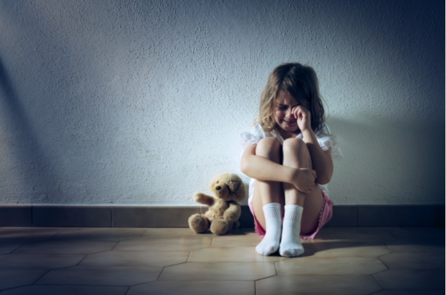 Sad child sitting on the floor hugging a teddy bear