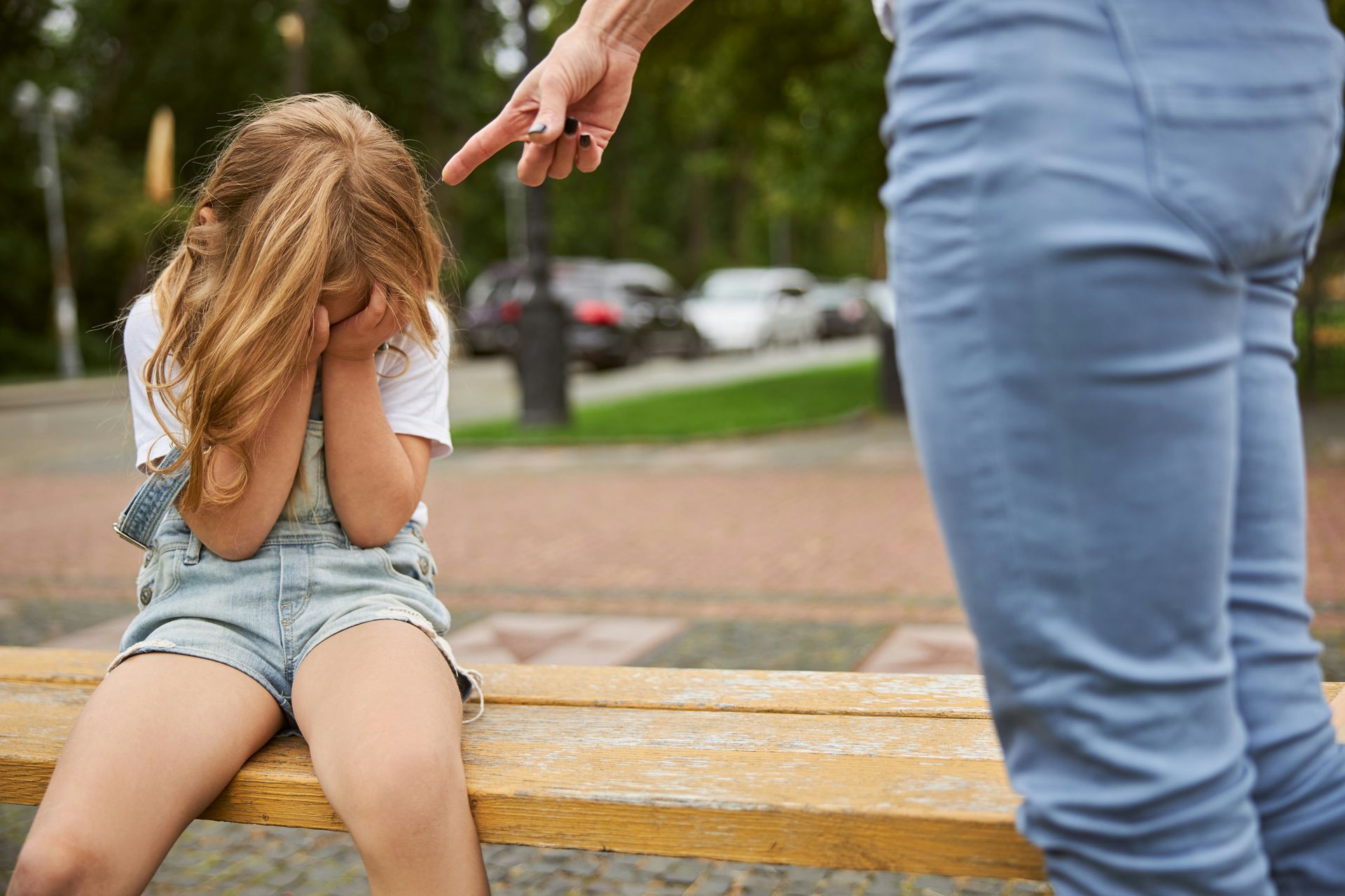 child sitting with her hands over her face and a parent pointing their finger at them