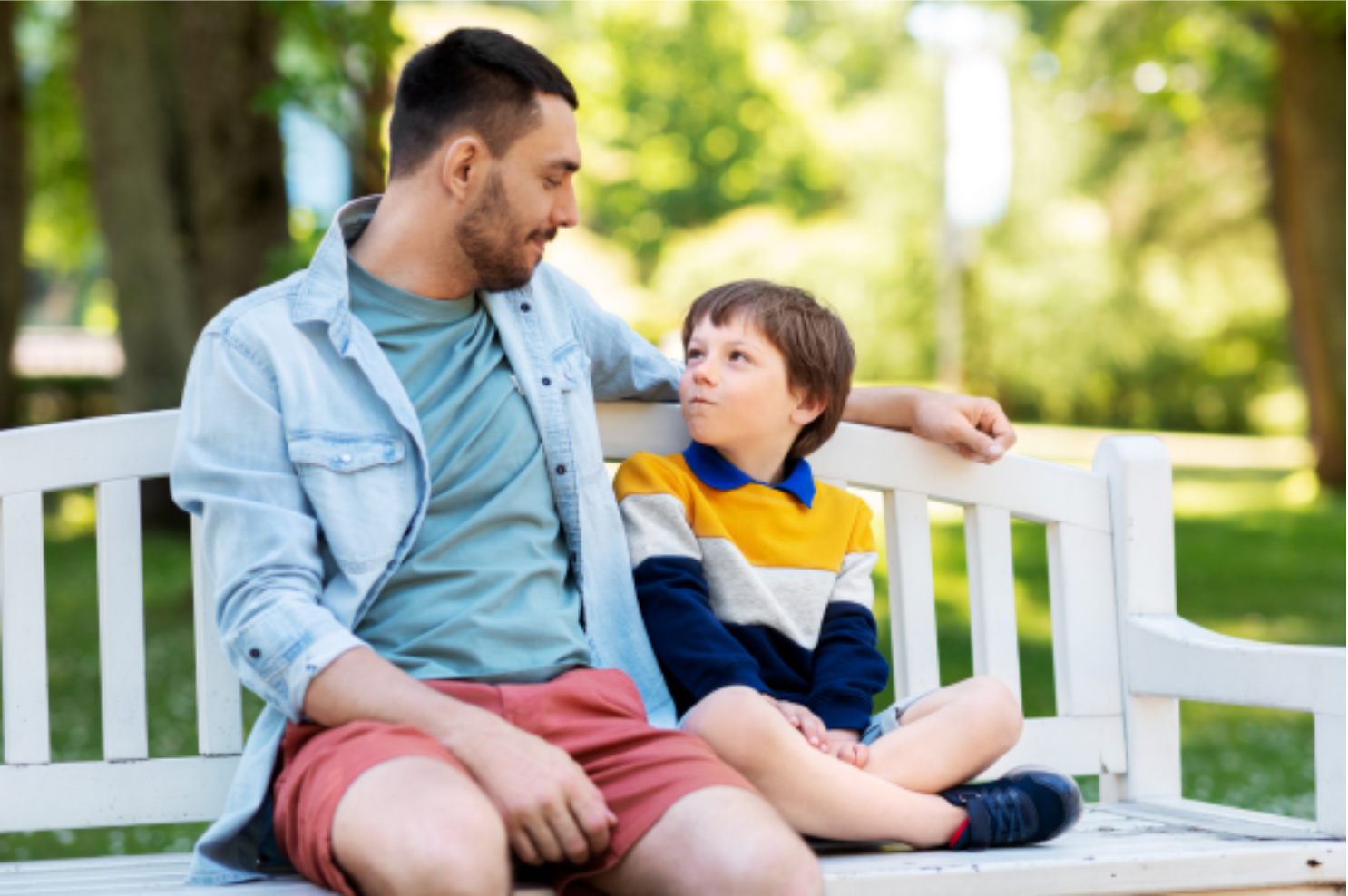 Father talking with his young son while sitting together on a park bench.