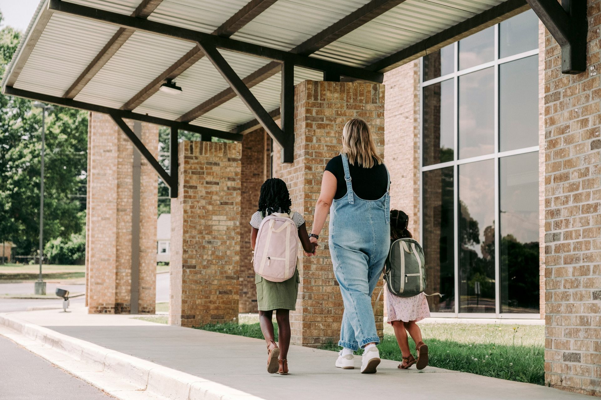 Children with backpacks walking toward a school entrance with their Mom