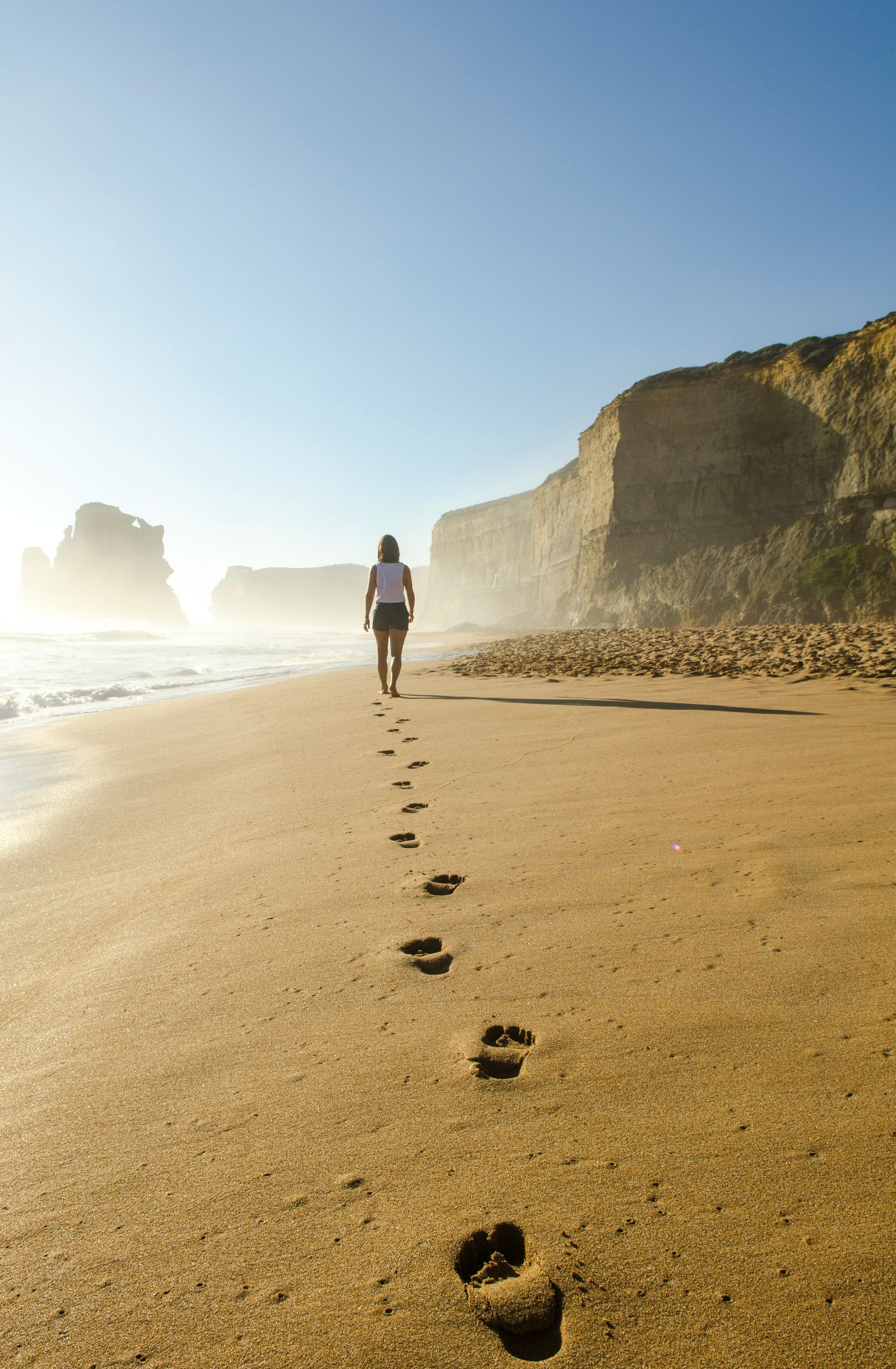 A person walking alone on a beach, leaving footprints in the sand. The image symbolizes healing, moving forward, and rebuilding self-trust one step at a time.