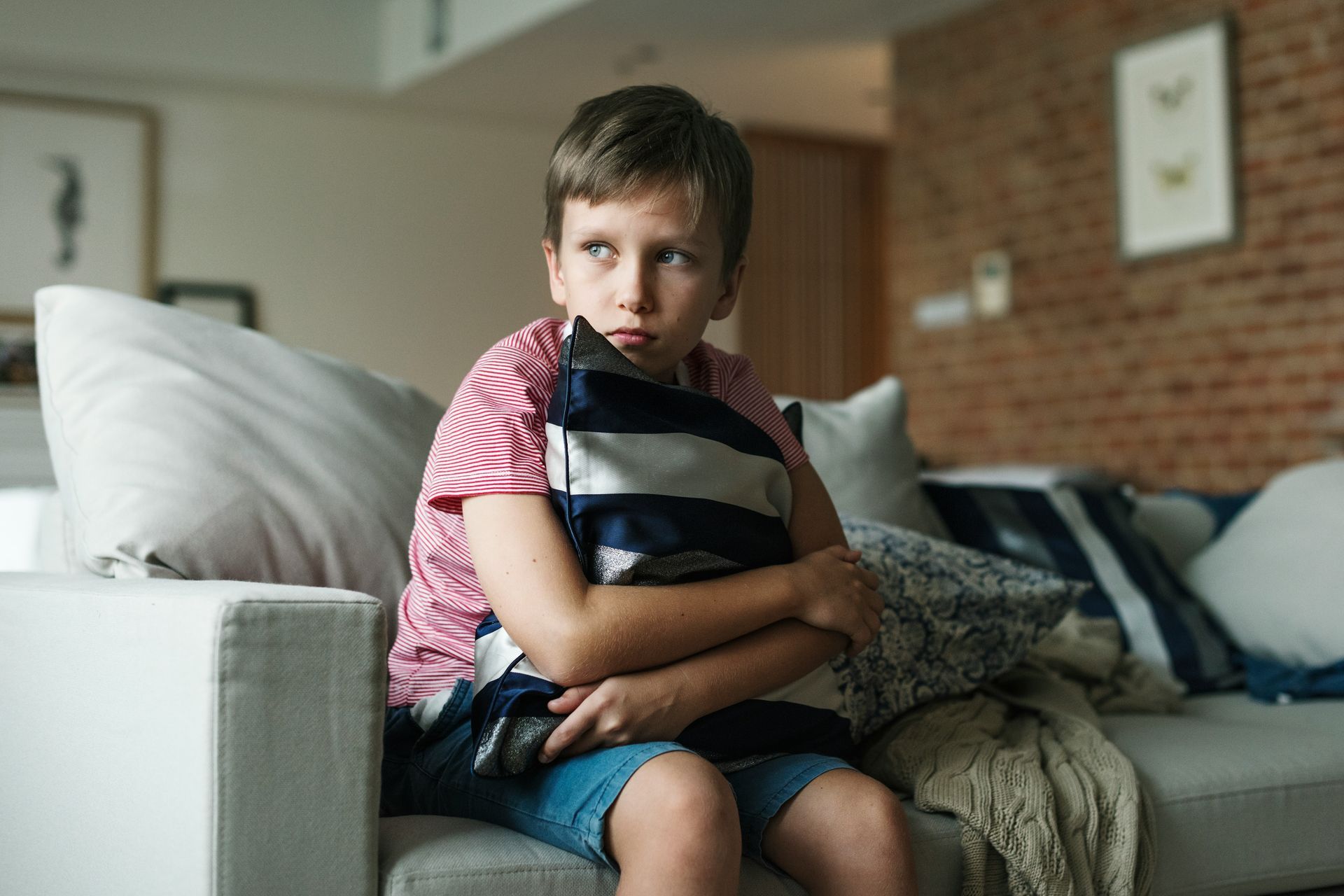 A young boy sits on a couch, clutching a pillow, showing the fear and uncertainty a child may feel around anger.