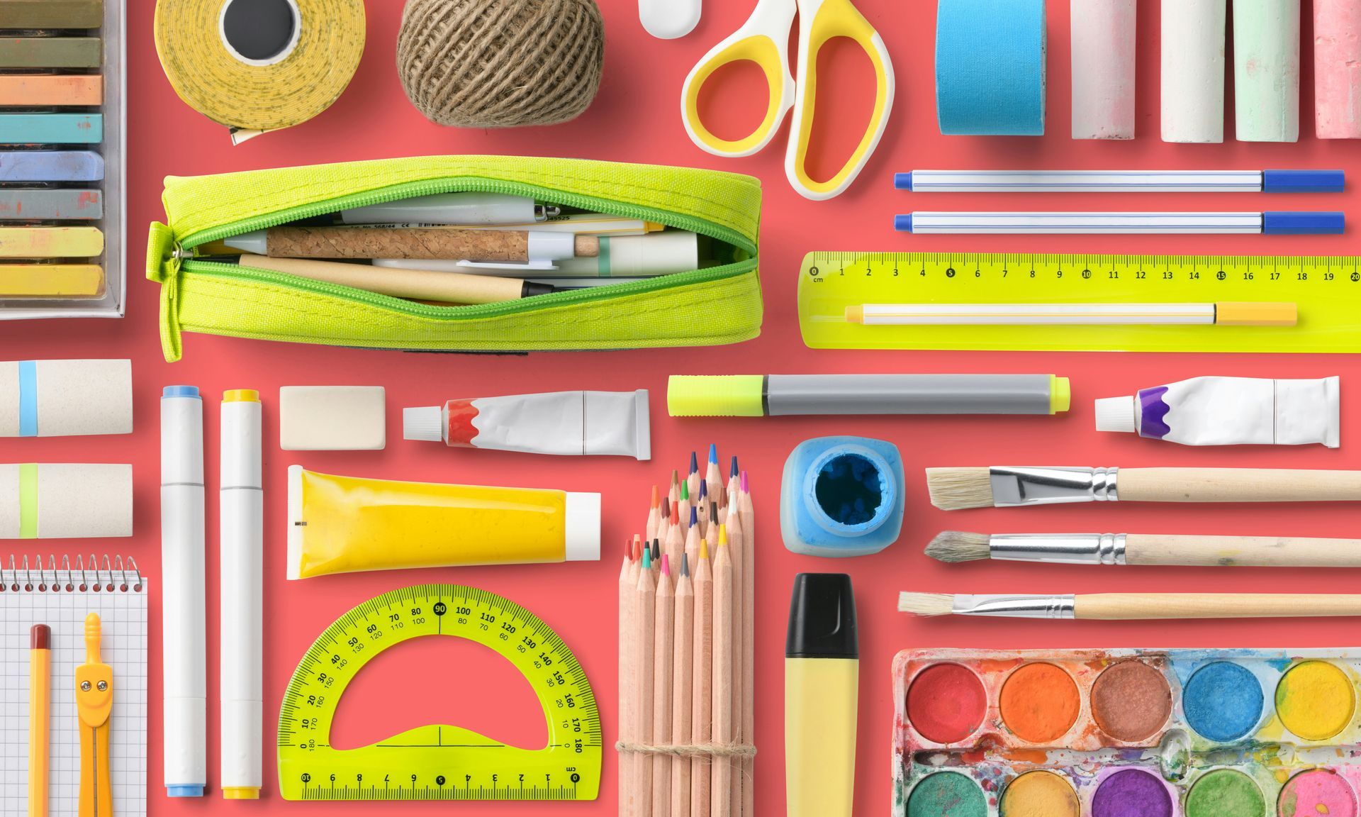 Colourful back-to-school supplies arranged on a red background, including pencils, markers, scissors, rulers, sticky notes and a pencil case.