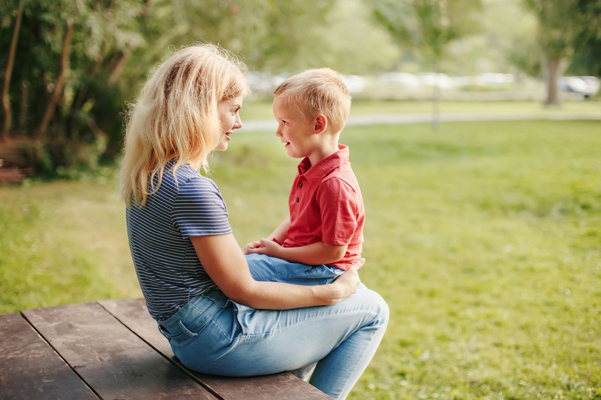 Adult kneeling at a child’s level and talking with them outdoors, showing the importance of listening to children and their needs.