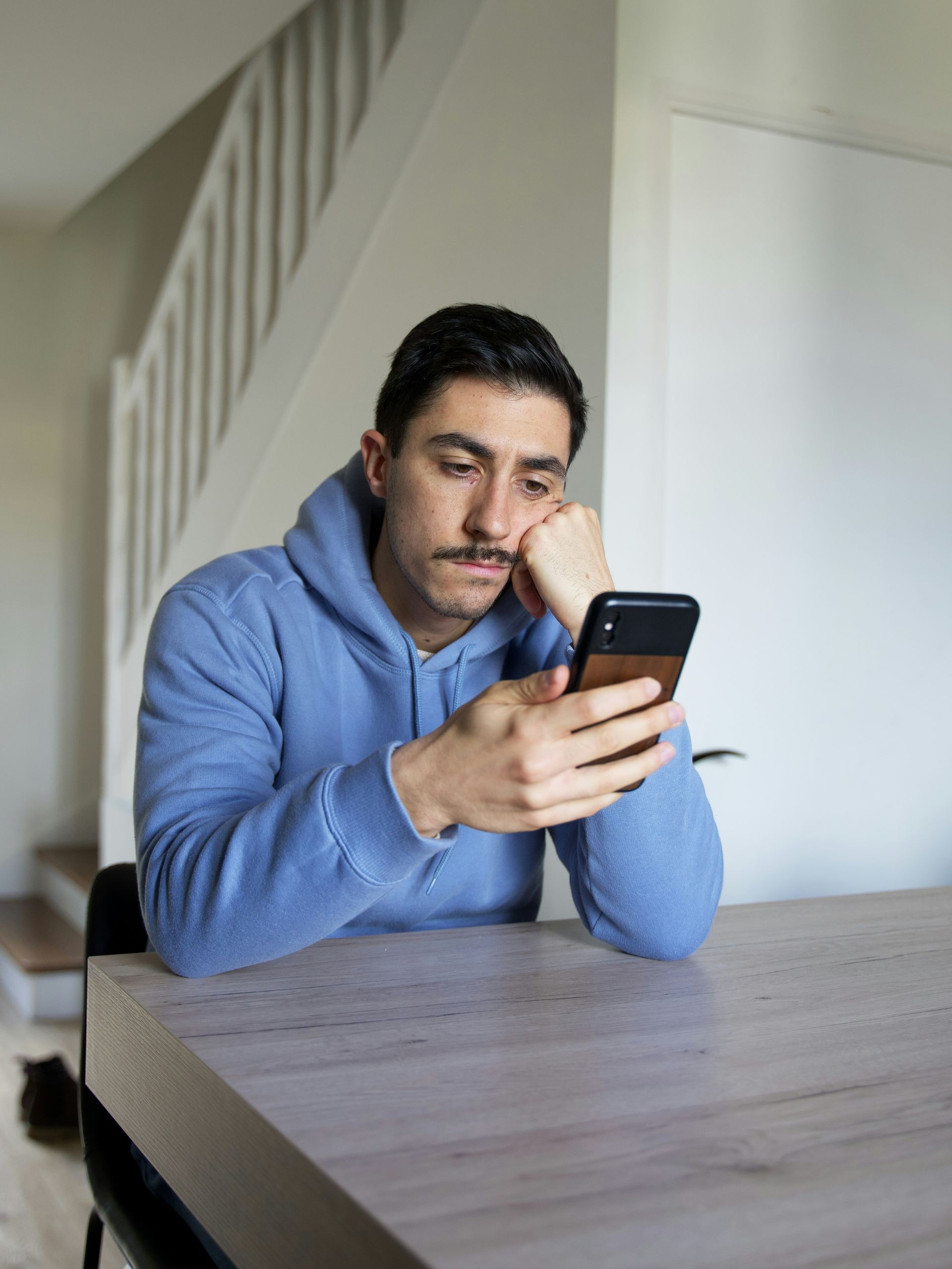 A person sitting at a table staring at their phone, waiting for a response that hasn’t come.