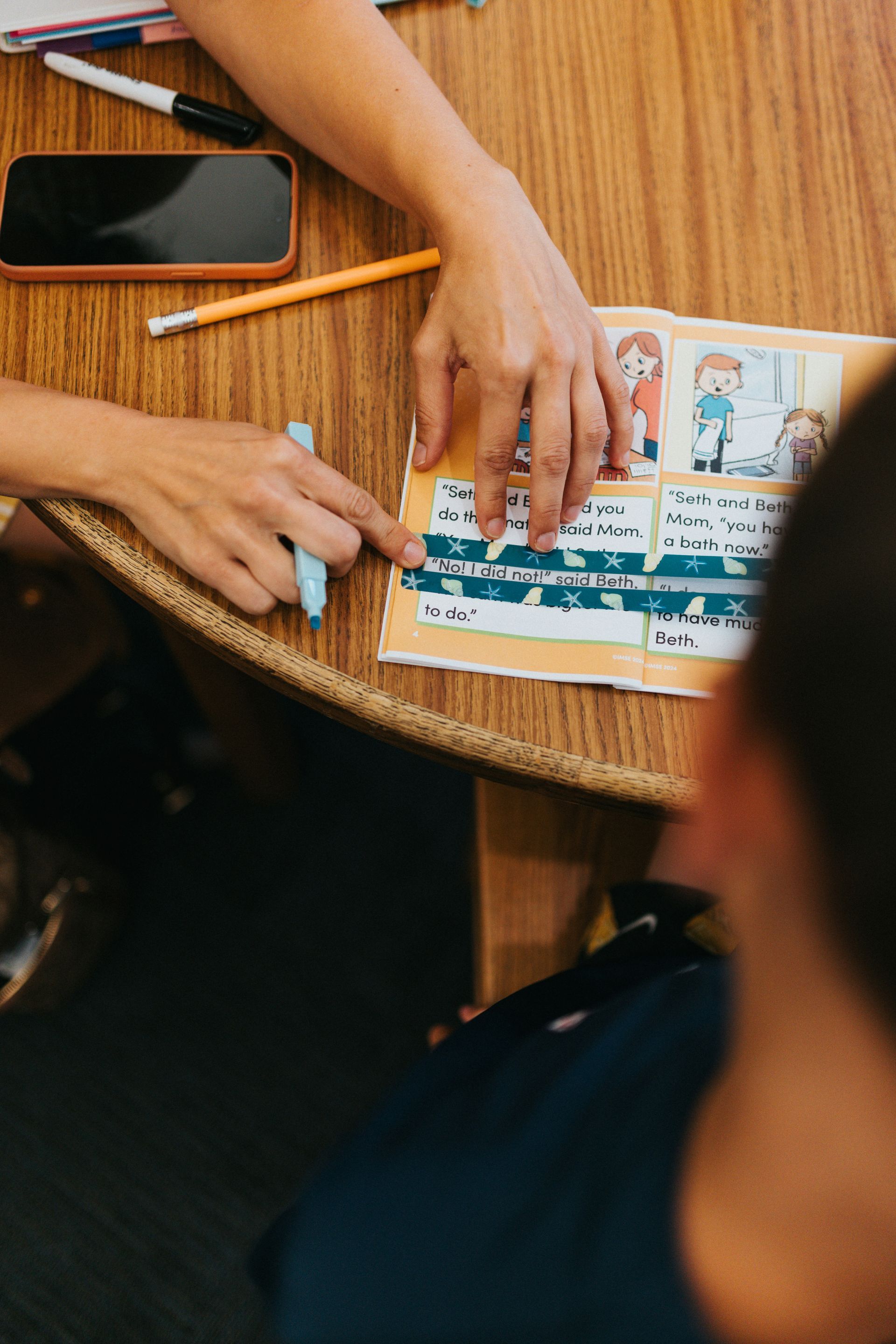 Child uses a reading window strip to focus on one line of text while an adult provides support during early reading practice.