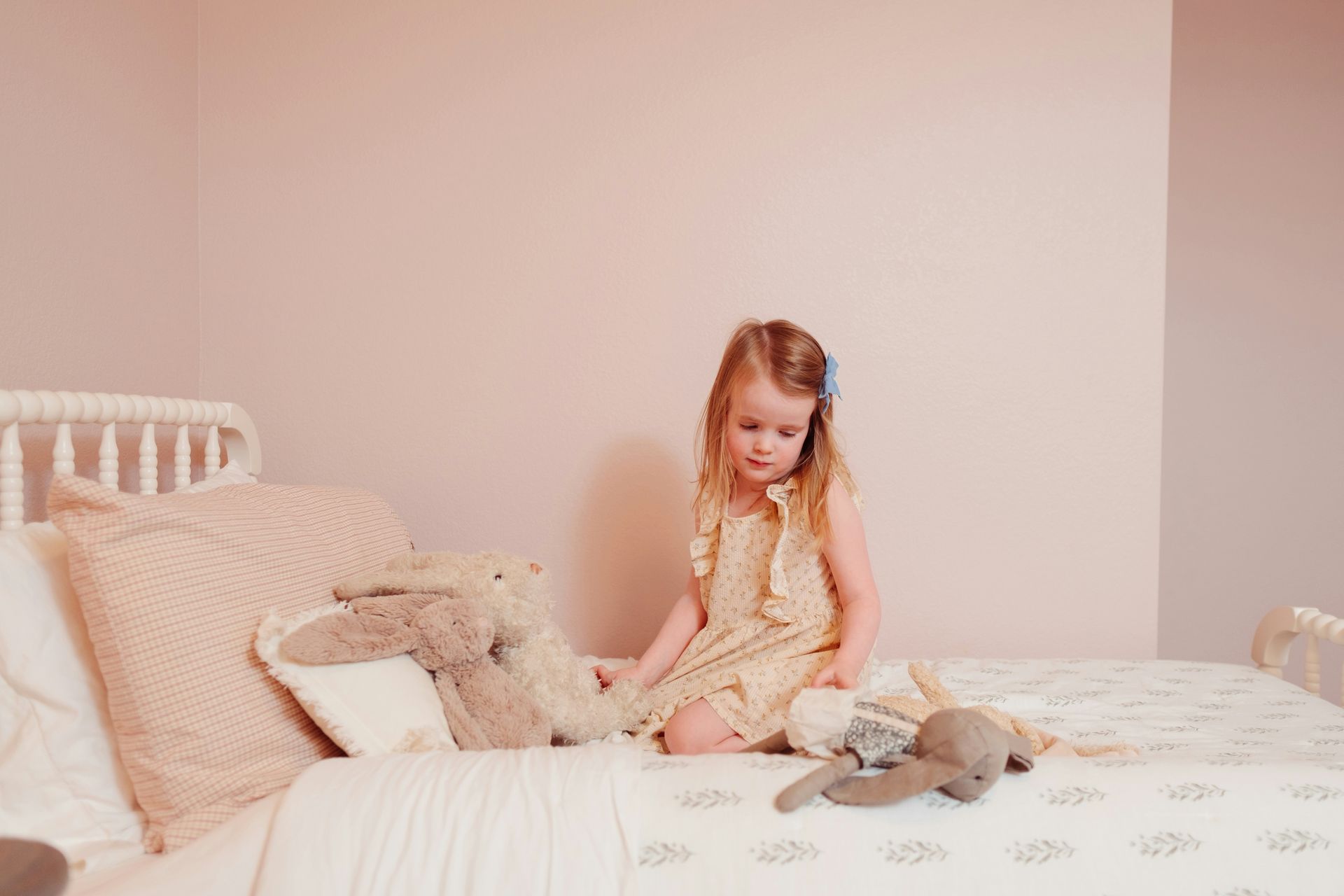 Young girl sitting alone on her bed, surrounded by stuffies, looking solemn