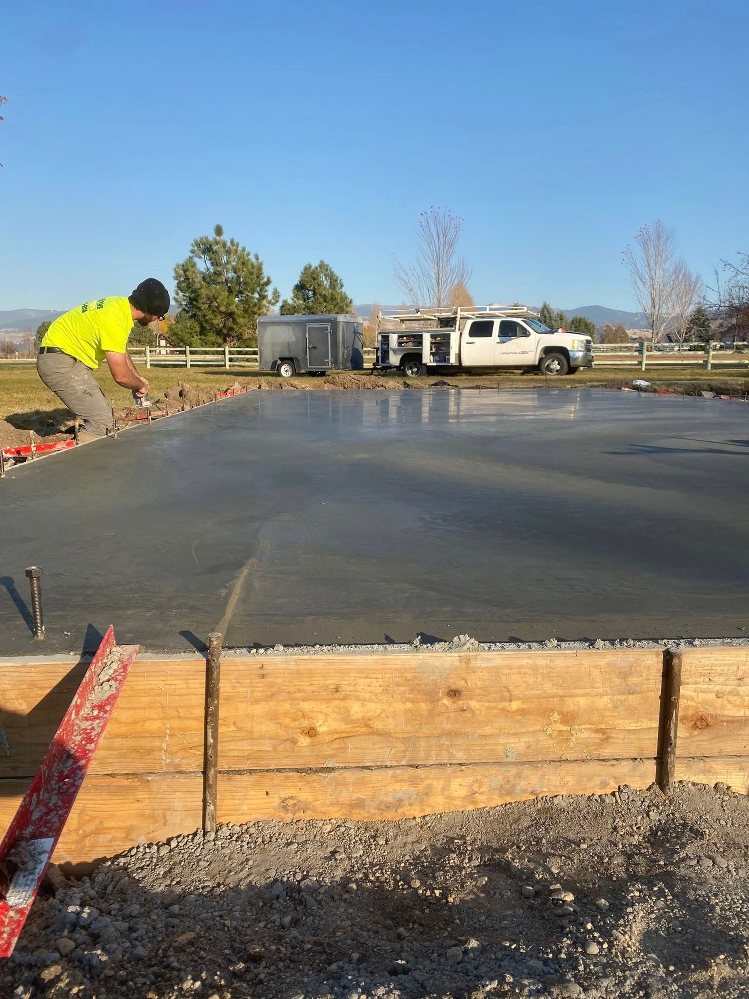 Worker pouring concrete slab at a construction site under a clear blue sky.