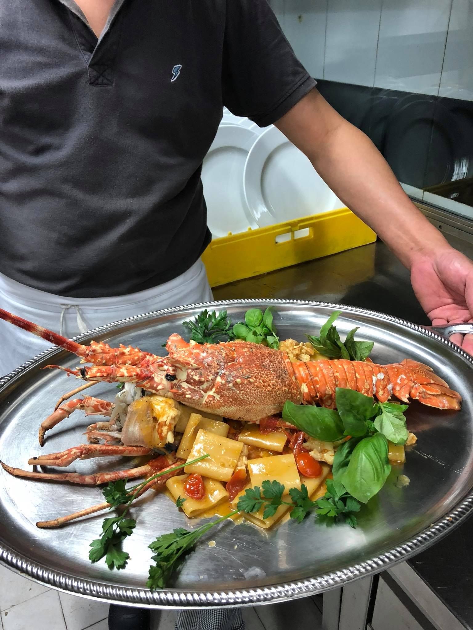 Un uomo tiene in mano un vassoio di cibo con sopra un'aragosta.