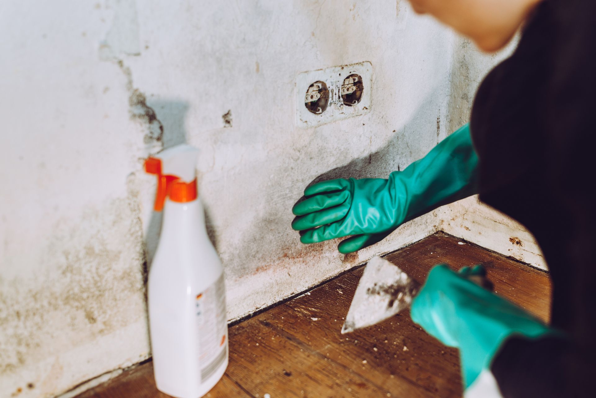 A person wearing green gloves is cleaning a wall with a spray bottle.