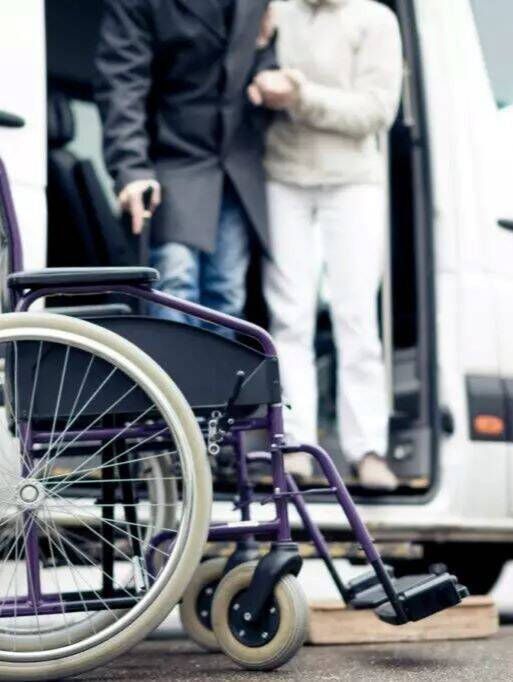 Wheelchair by a vehicle doorway, with two people standing nearby.