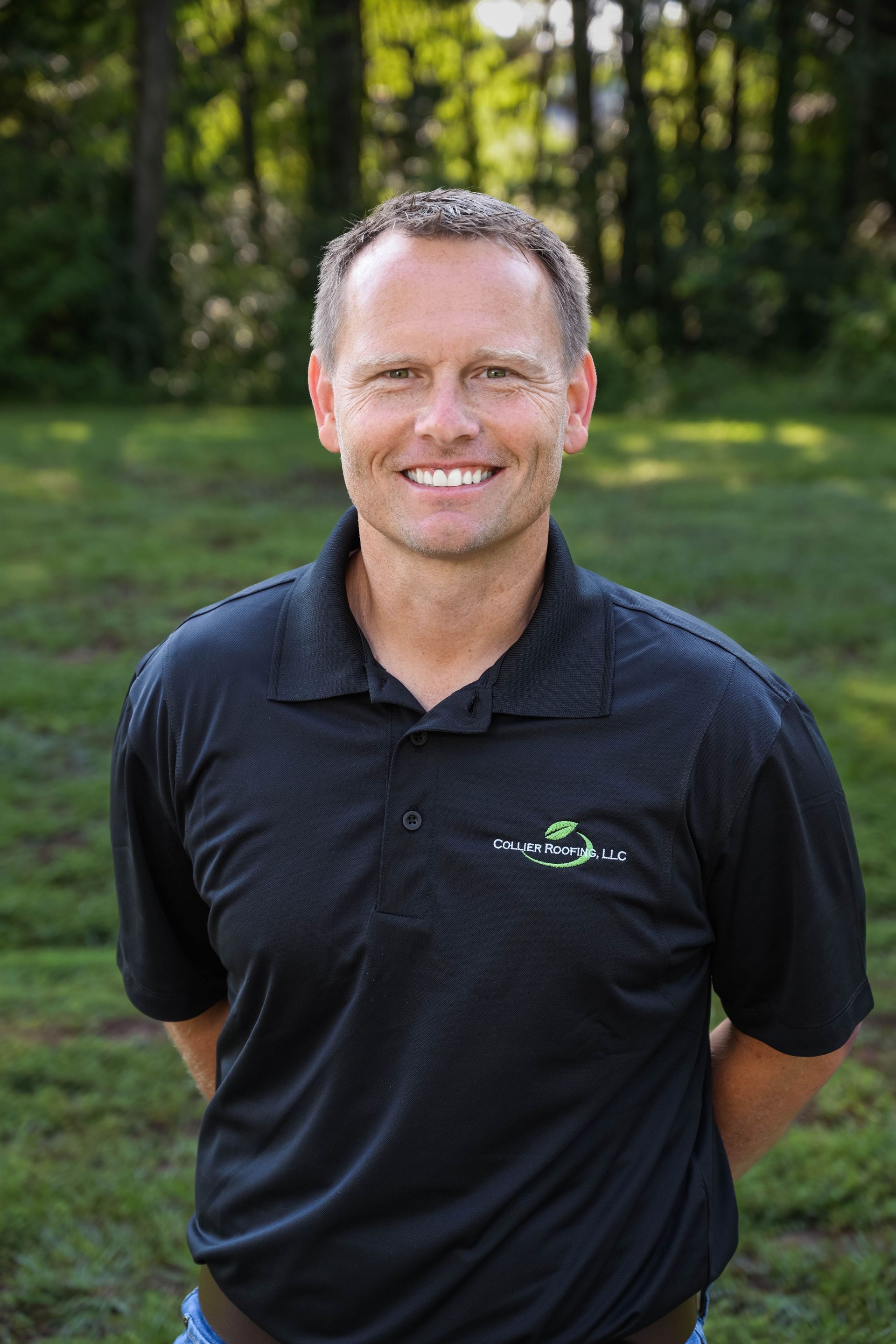 A man in a black shirt is smiling for the camera while standing in the grass.