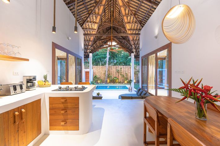 Open-plan kitchen and dining area with high, vaulted wooden ceilings, leading to an outdoor pool and lush garden.