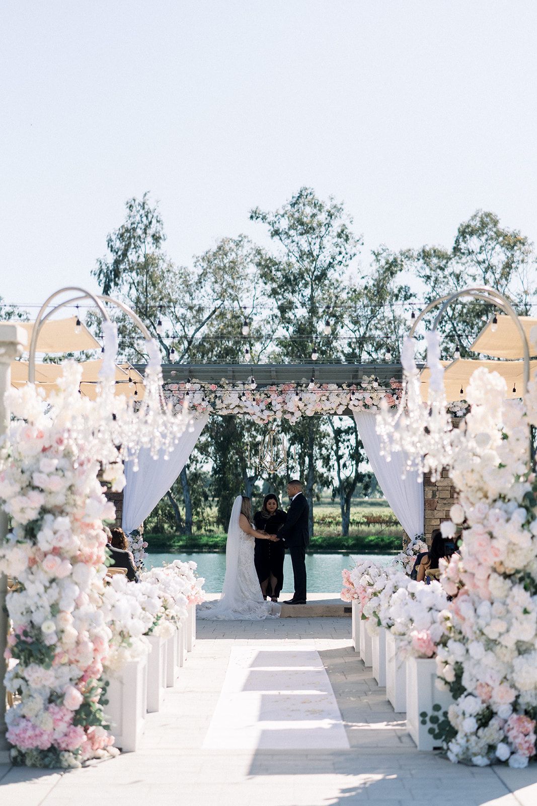 A bride and groom are standing under a chandelier at their wedding ceremony.
