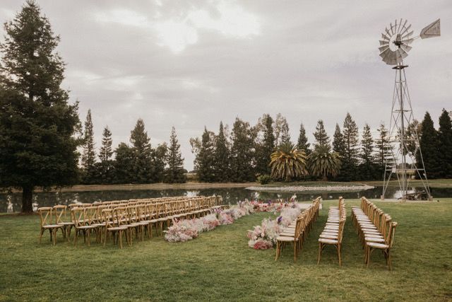 outdoor seating with wooden chairs on lakefront lawn line with flower arrangements awaiting marriage ceremony