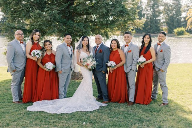 bride and groom centered between alternating bridal party and groomsmen wearing red dresses and gray suits with matching red pocket squares