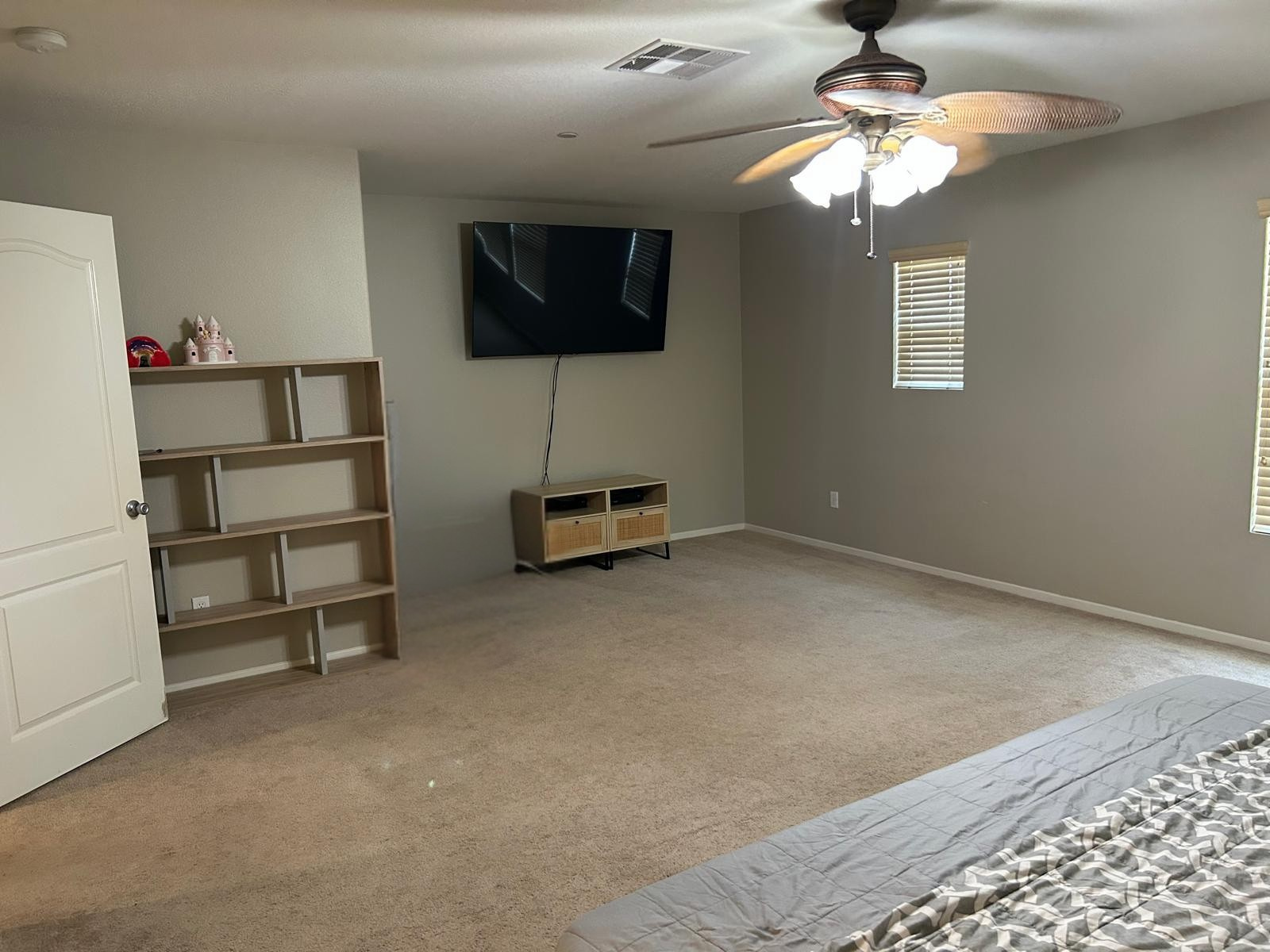 A bedroom with a ceiling fan and a flat screen tv