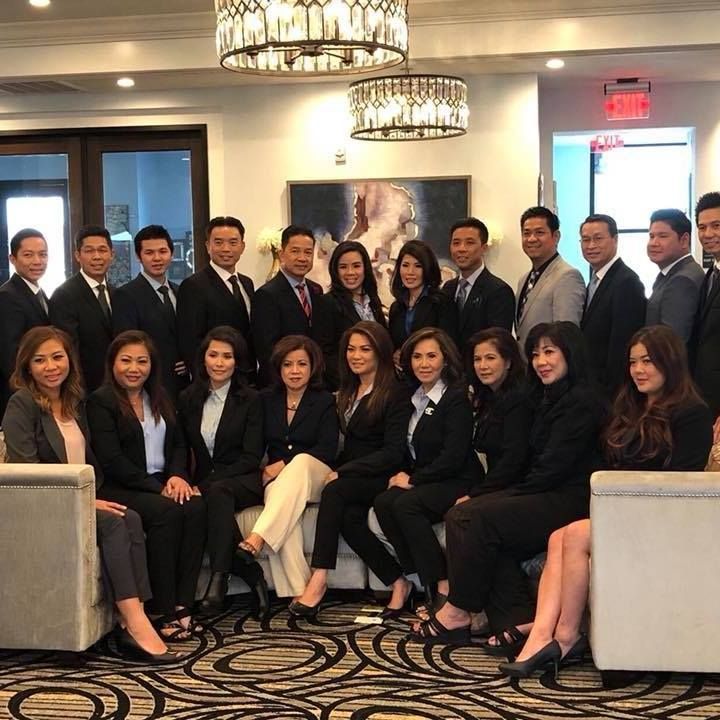 A large group of professionals in business attire pose for a formal group portrait in a brightly lit, elegant lobby.