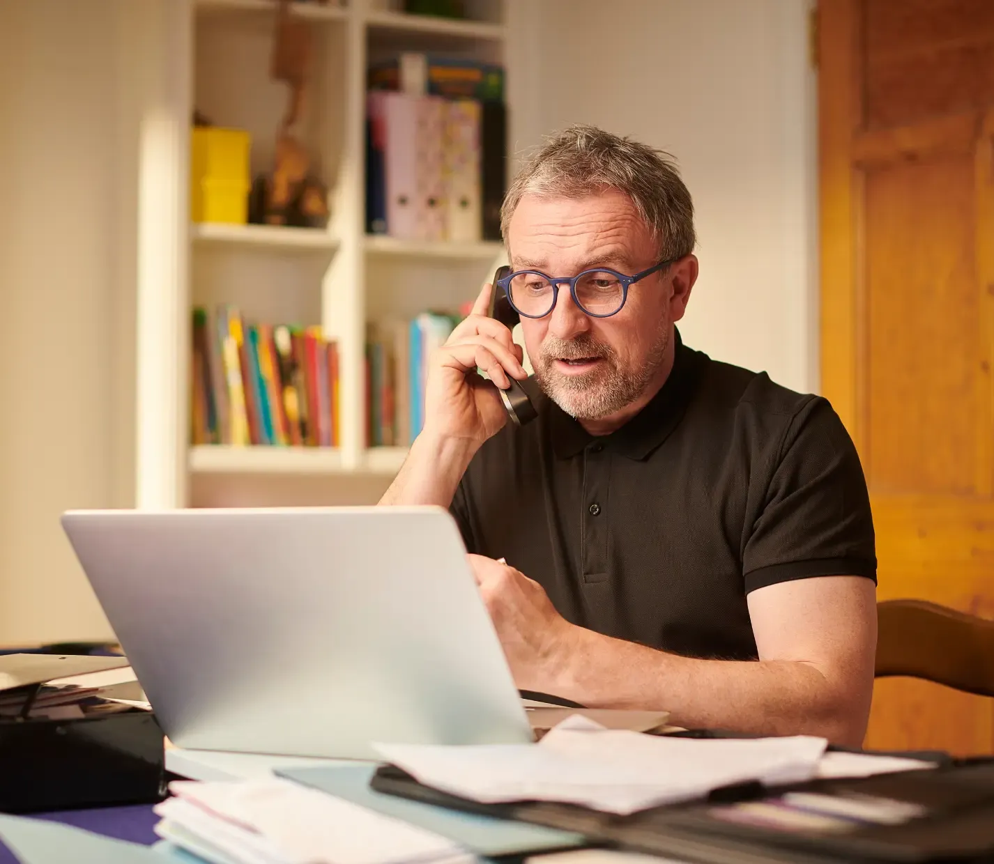 Man on a phone call working at a laptop in a warm home office