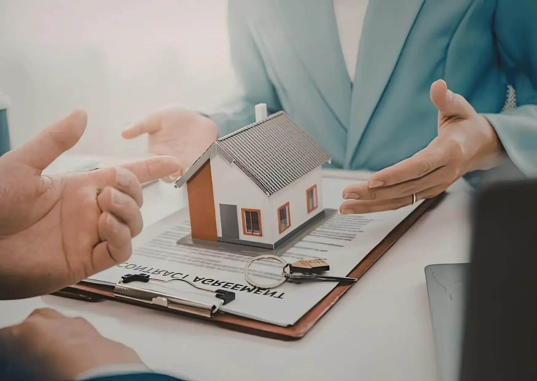 Hands presenting a small house model on a clipboard during a real estate meeting