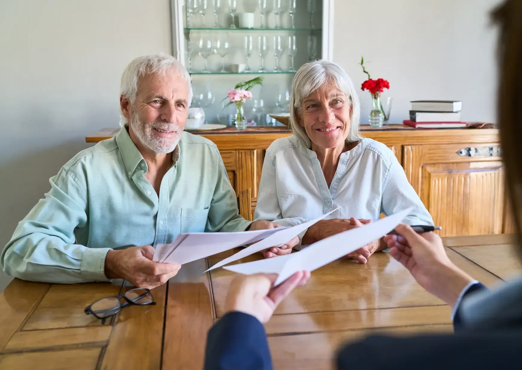 Two smiling seniors meet with a counselor at a table in a bright room, reviewing documents.