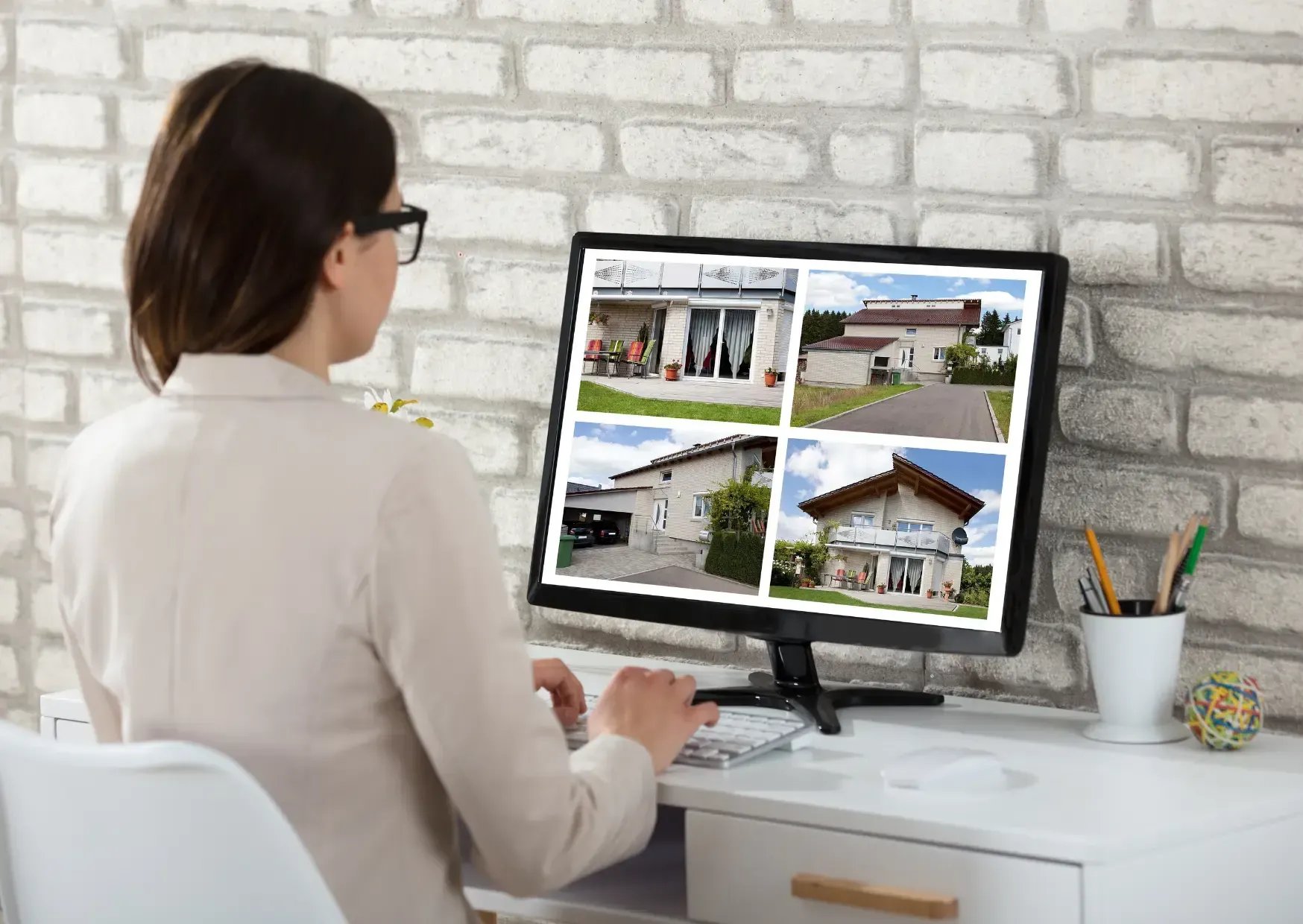 Person using a desktop computer to view house photos in a bright home office