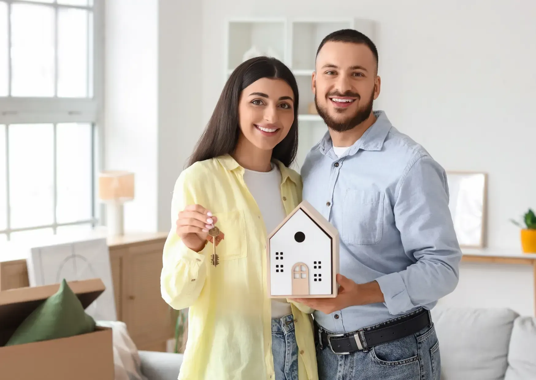 Two people smiling and holding a small house model in a bright room