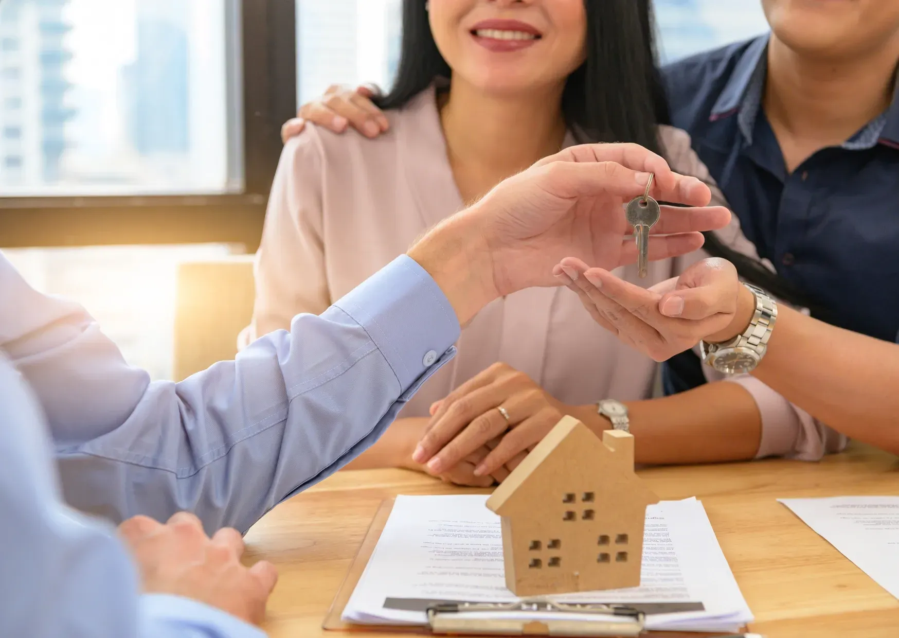 Hands passing a small house model over documents at a desk during a meeting