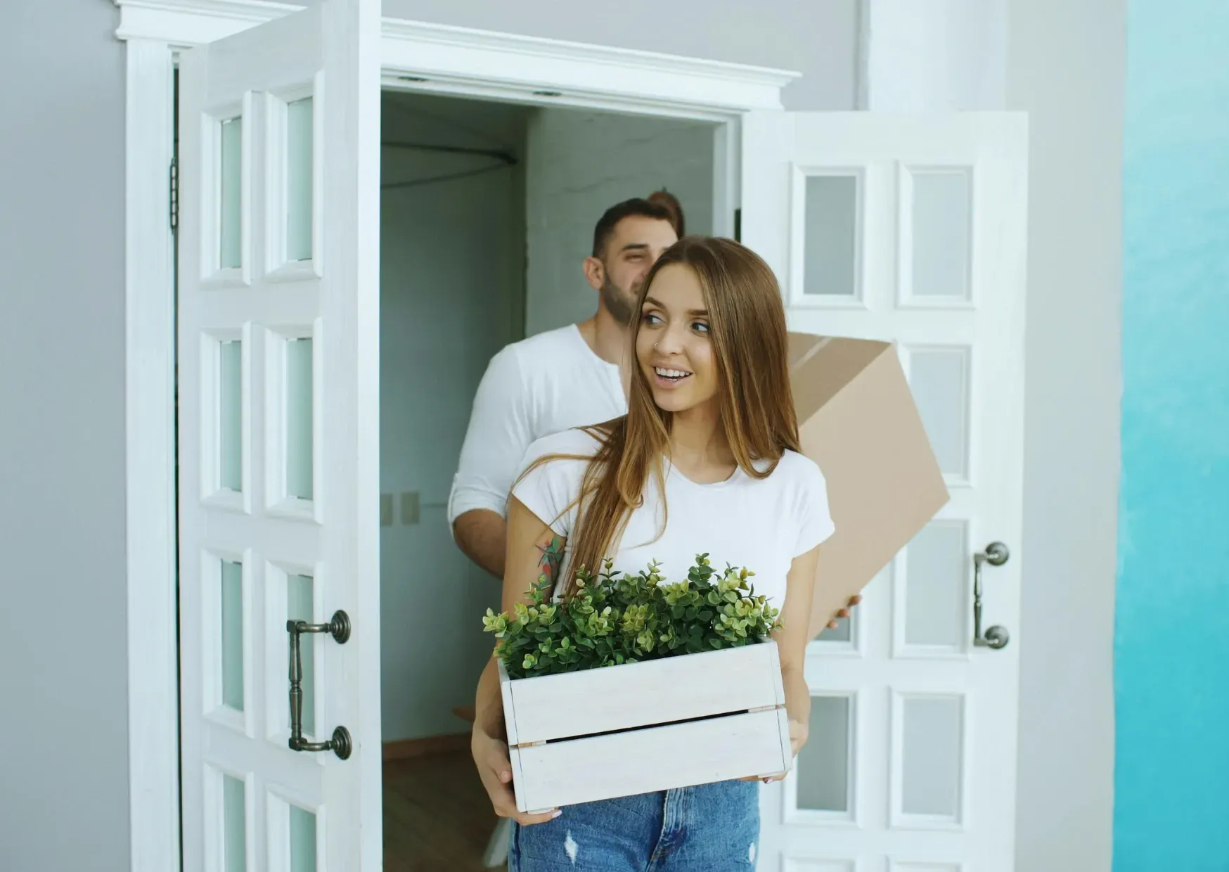 People carrying moving boxes into a bright home through an open front door