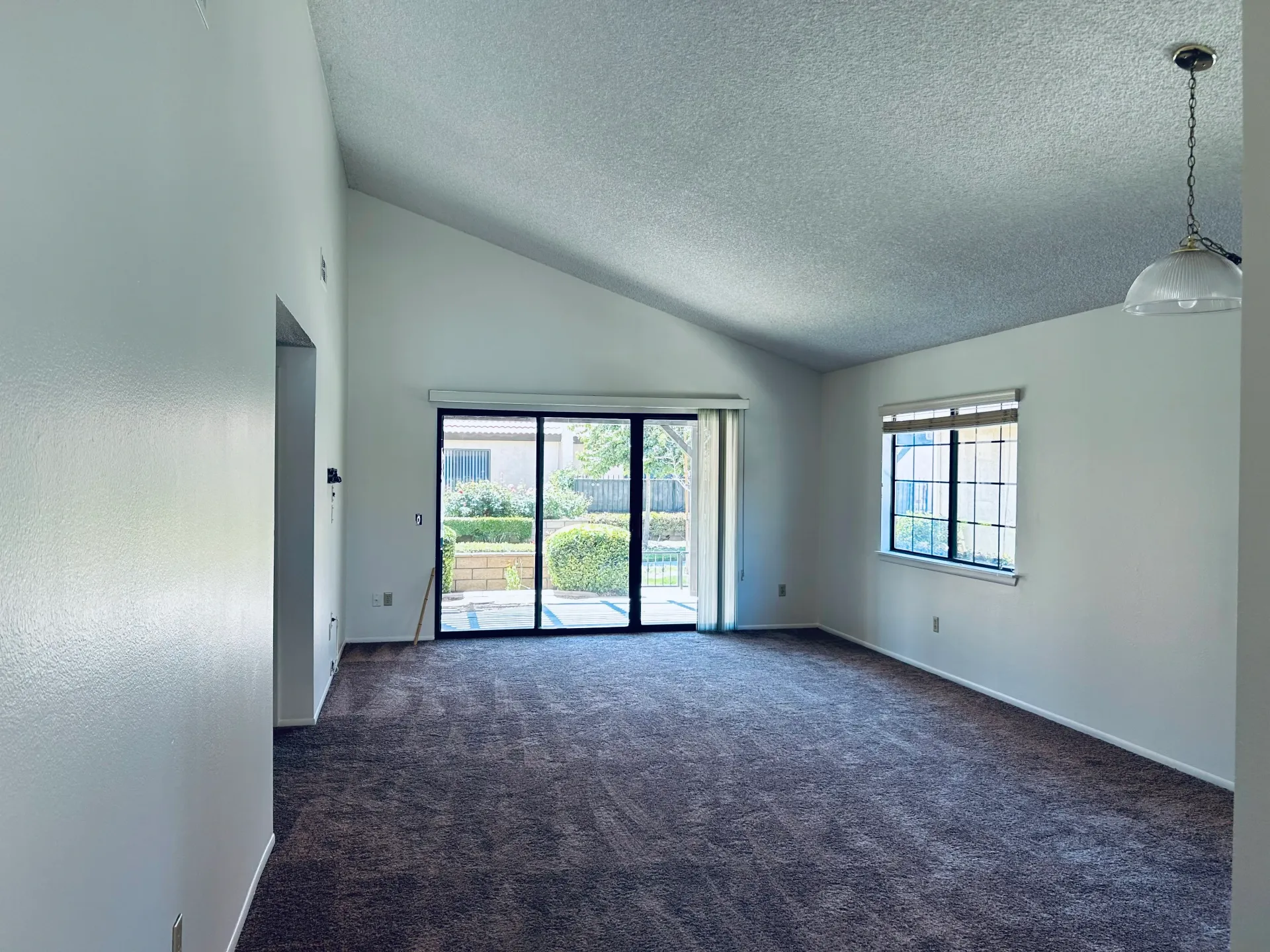 An empty living room with a vaulted ceiling and sliding glass doors.