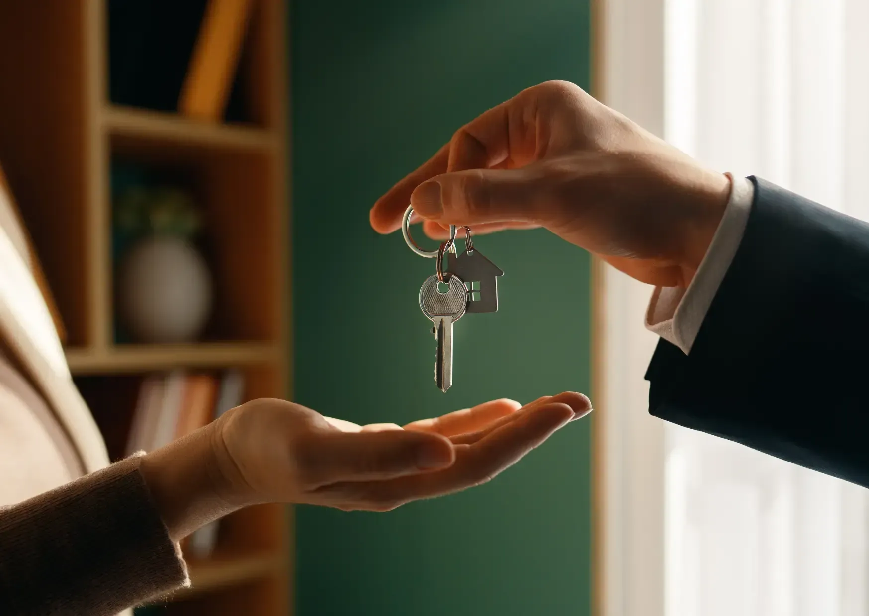 Handing over a house key between two people indoors, symbolizing a property exchange
