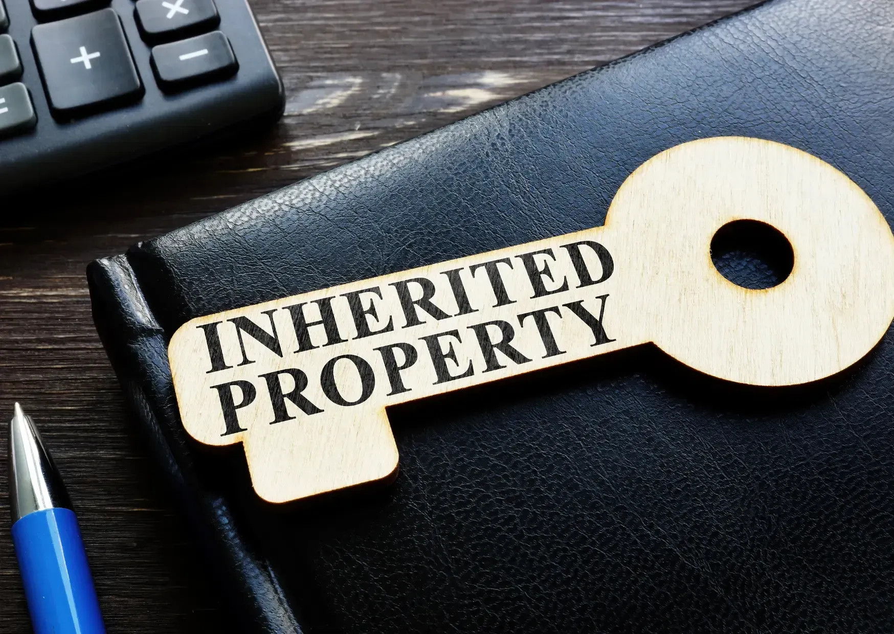 Gold key labeled “Inherited Property” beside a pen on a desk