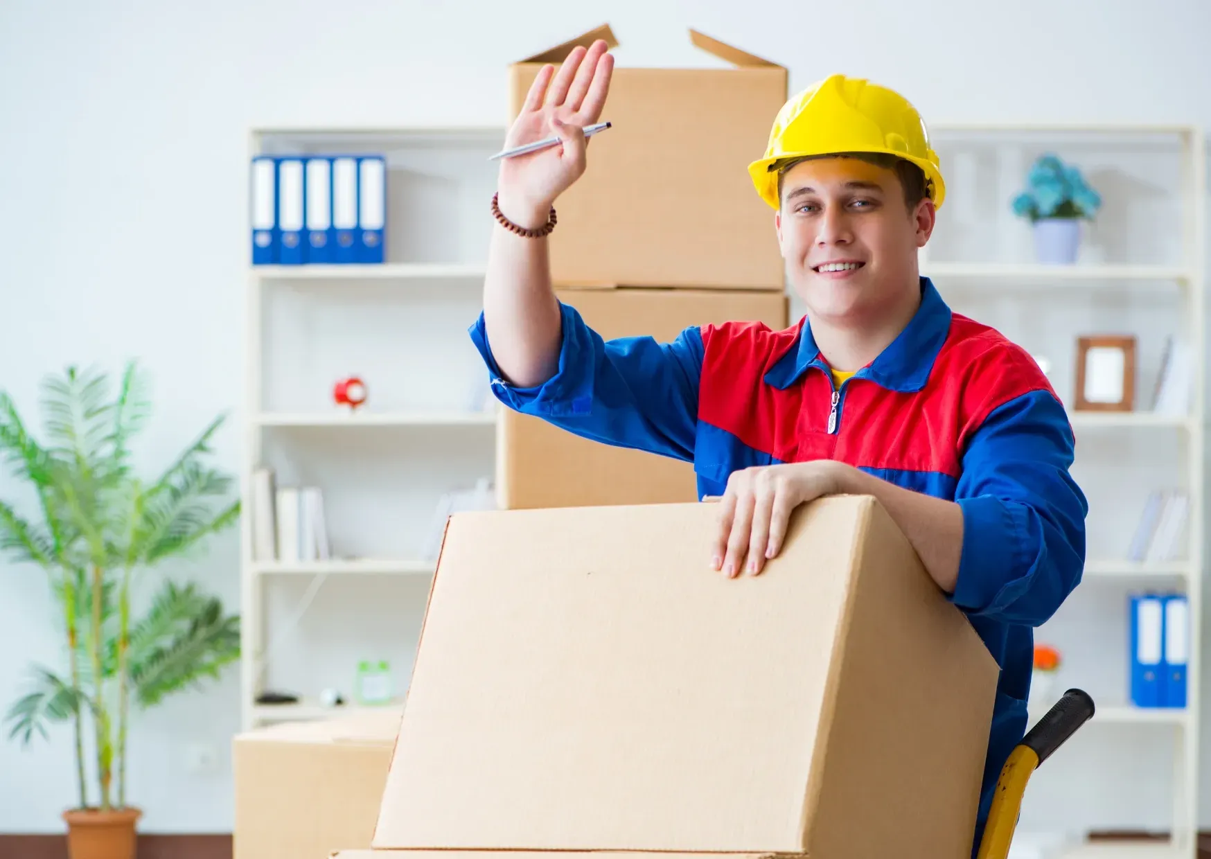 Delivery worker in yellow hard hat holding a parcel in a bright office