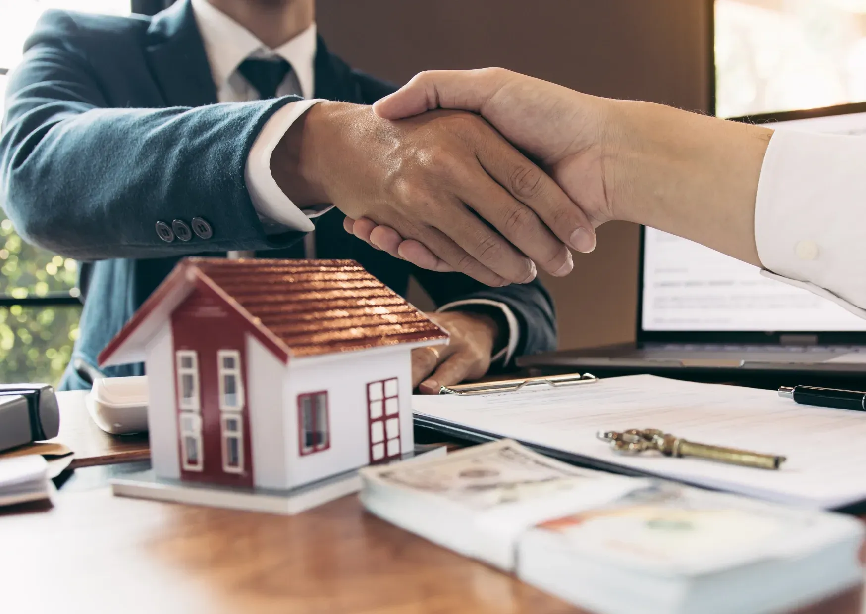 Handshake over house model and contract documents on a desk