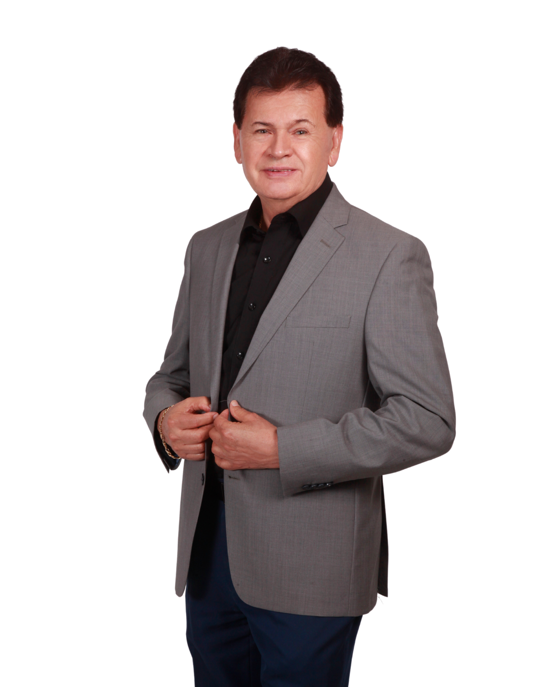 Man in gray blazer and black shirt smiling, hands on jacket.