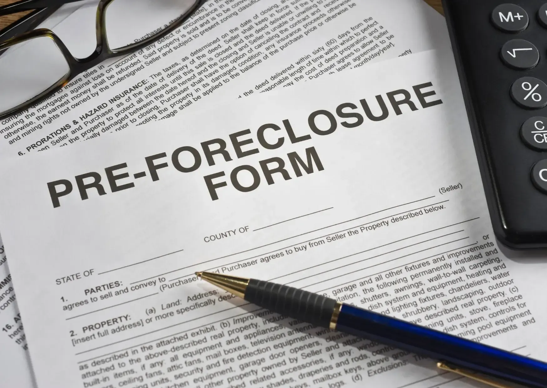 Pre-foreclosure form on desk with pen, glasses, and calculator nearby