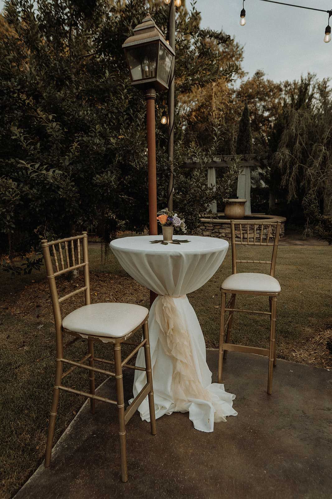 A small table with a white cloth skirt, two gold chairs, and a streetlamp outdoors.