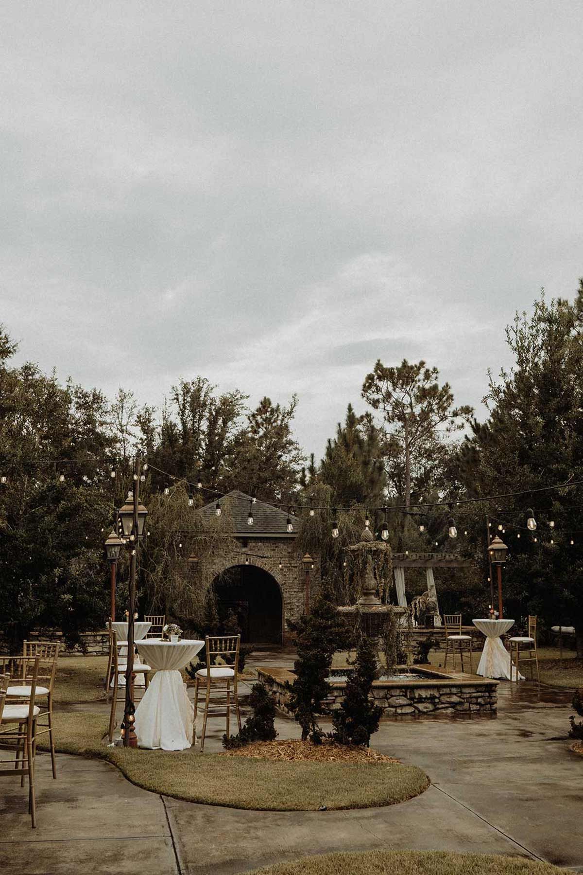 Outdoor wedding venue with chairs, tables, and a stone structure under a cloudy sky.