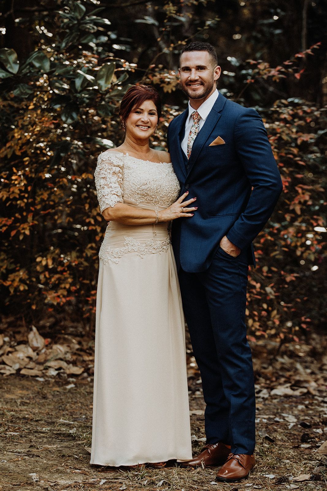 Woman in gold dress and man in blue suit pose outdoors, smiling.