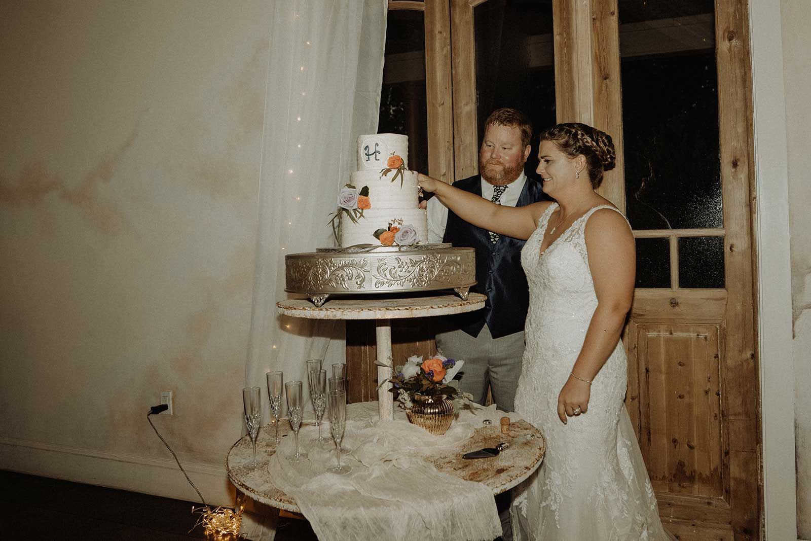 Couple cuts a wedding cake at a reception. Cake is tiered, decorated with flowers.