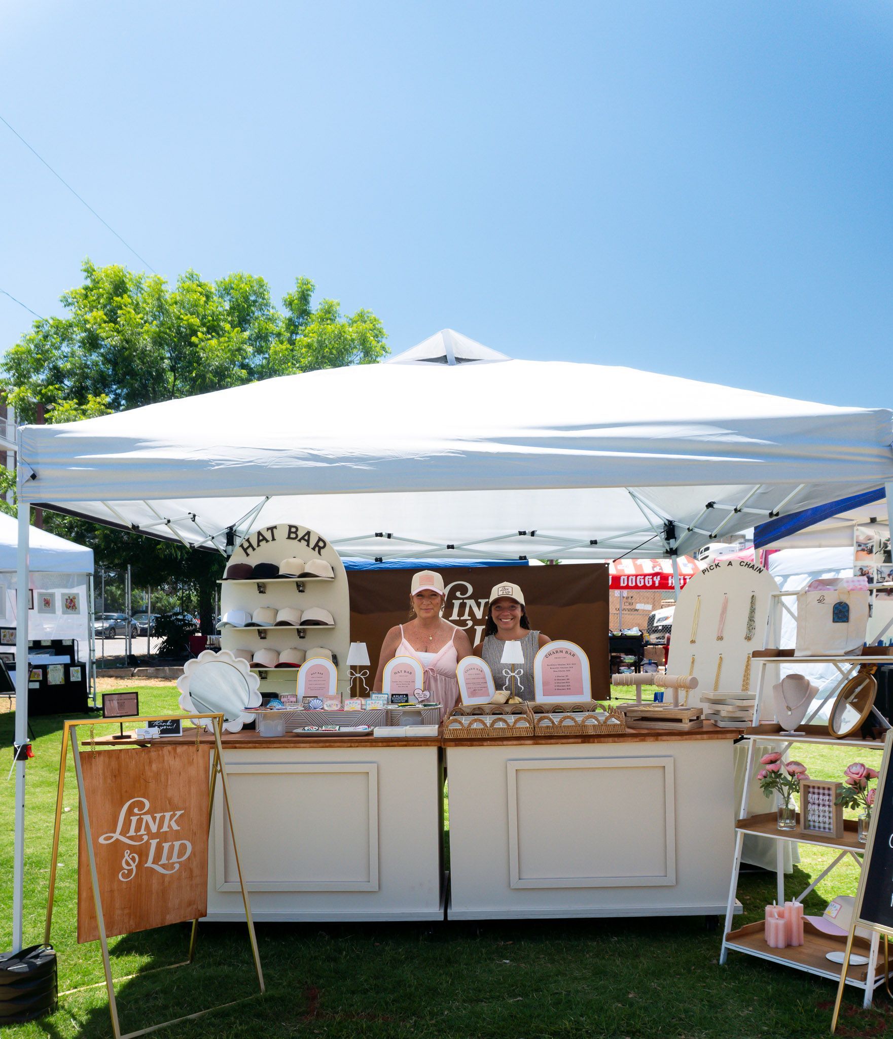 The owners of Link & Lid standing in front of their custom hat and charm bar booth during Bishop Bazaar.