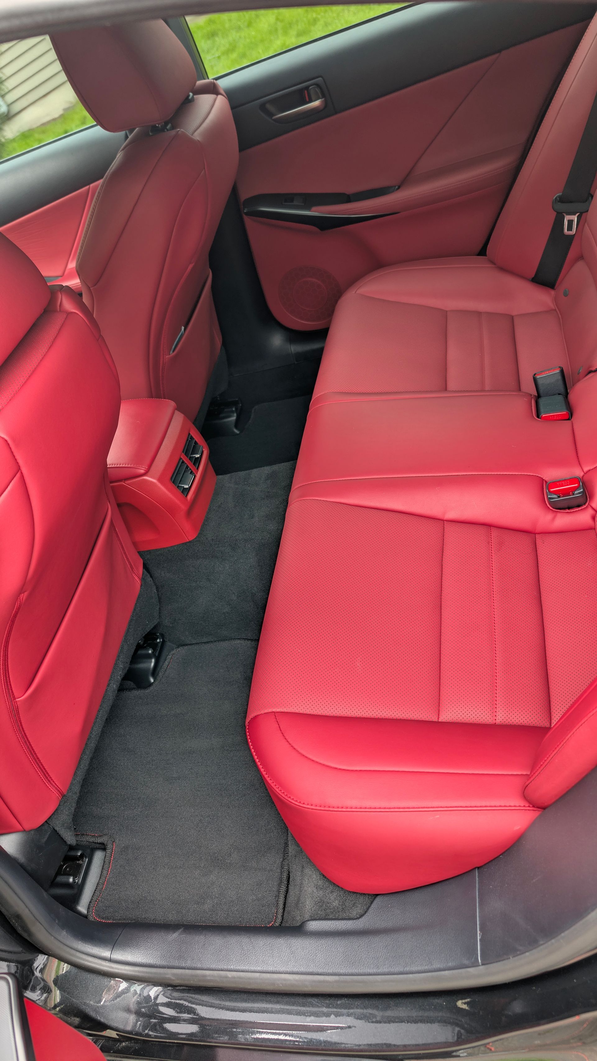 Red car back seat with red upholstery, black floor mats, and rear door open