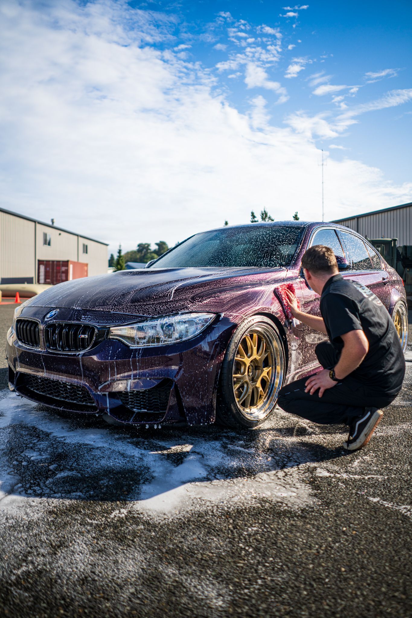 Person washing a dark red sports car with soap and water outdoors at a car wash.