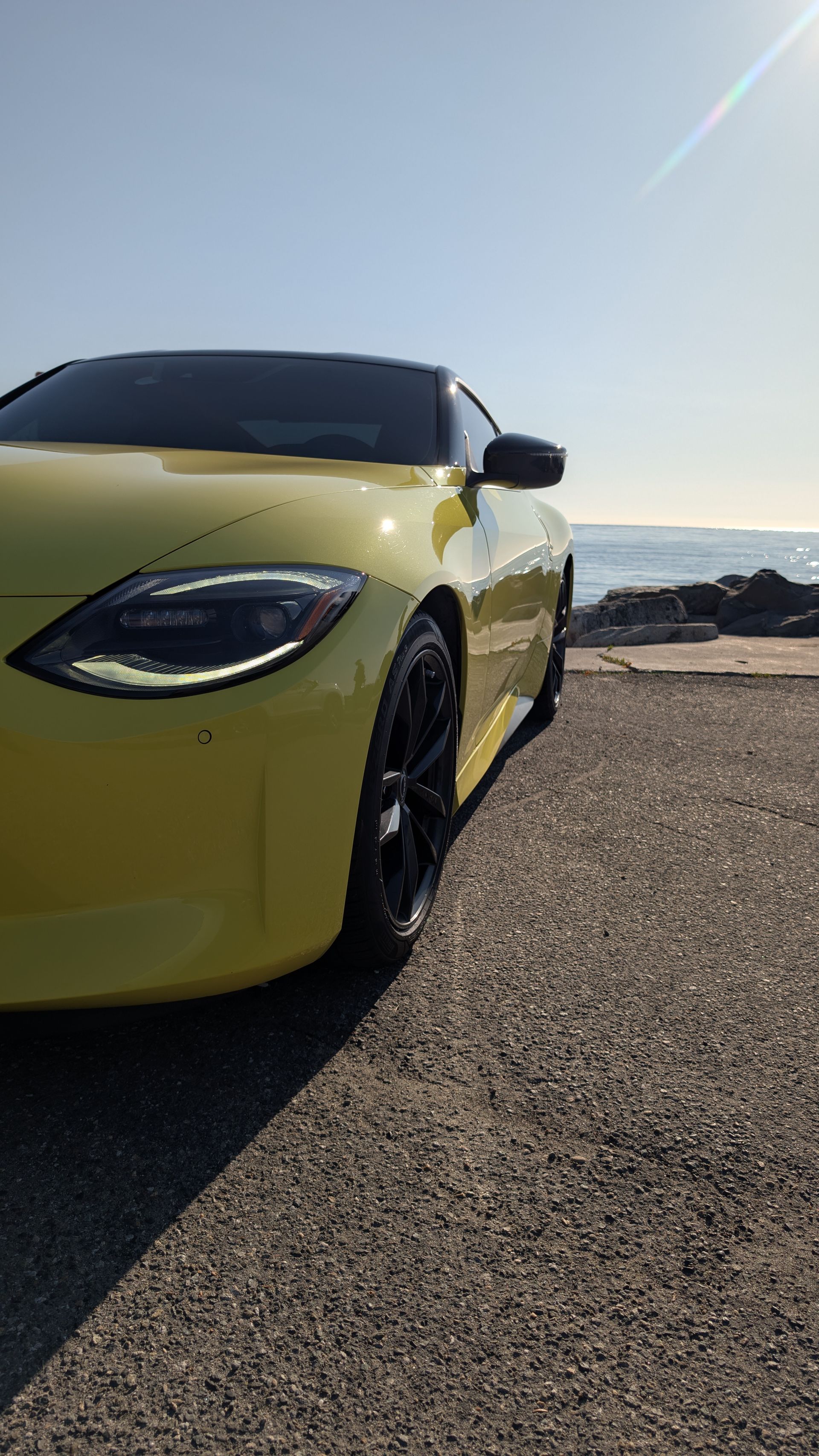Yellow sports car parked by the roadside under a bright sky, front-left view