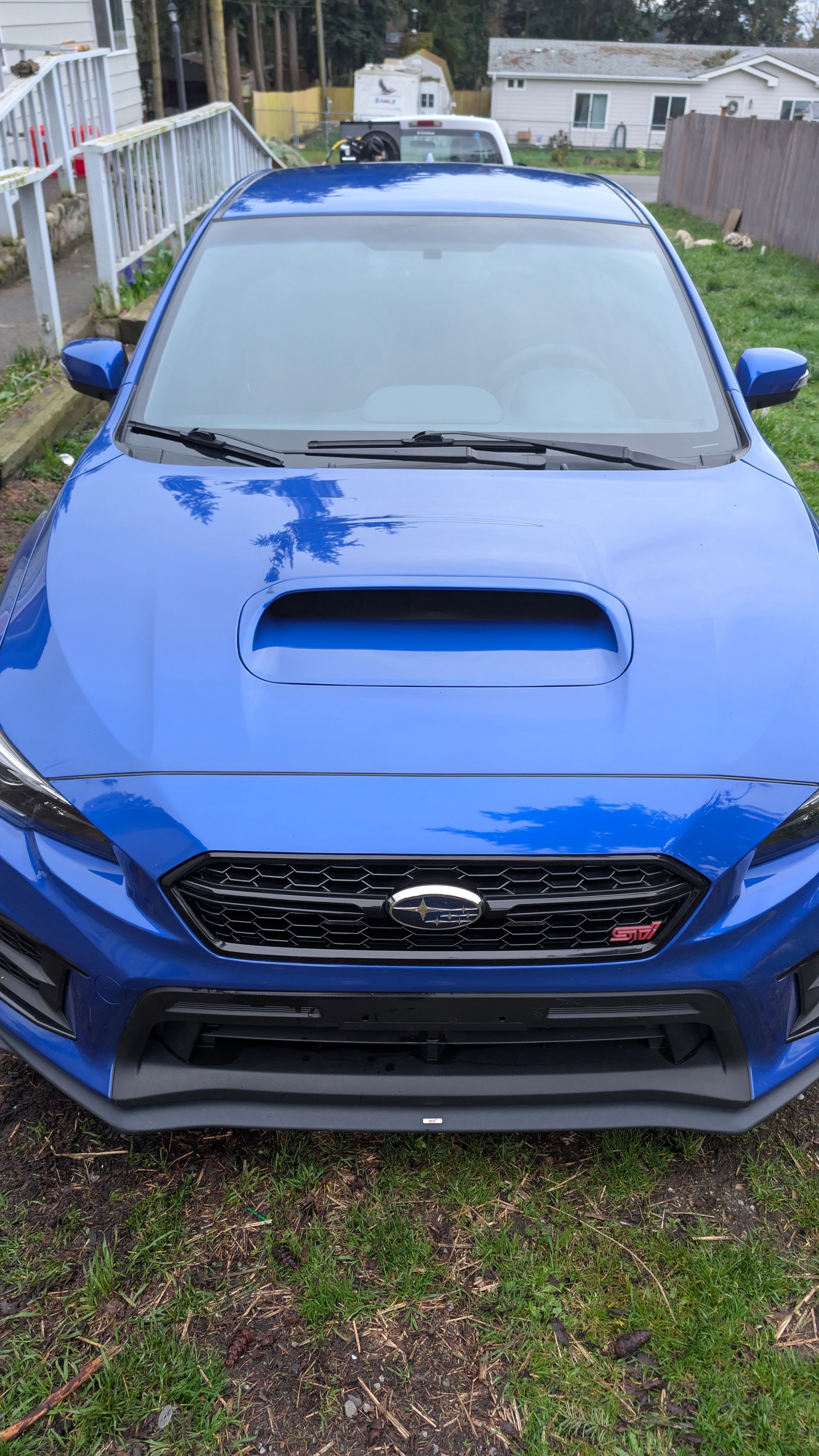 Blue Subaru parked on a grassy driveway, front view with hood scoop and grille visible