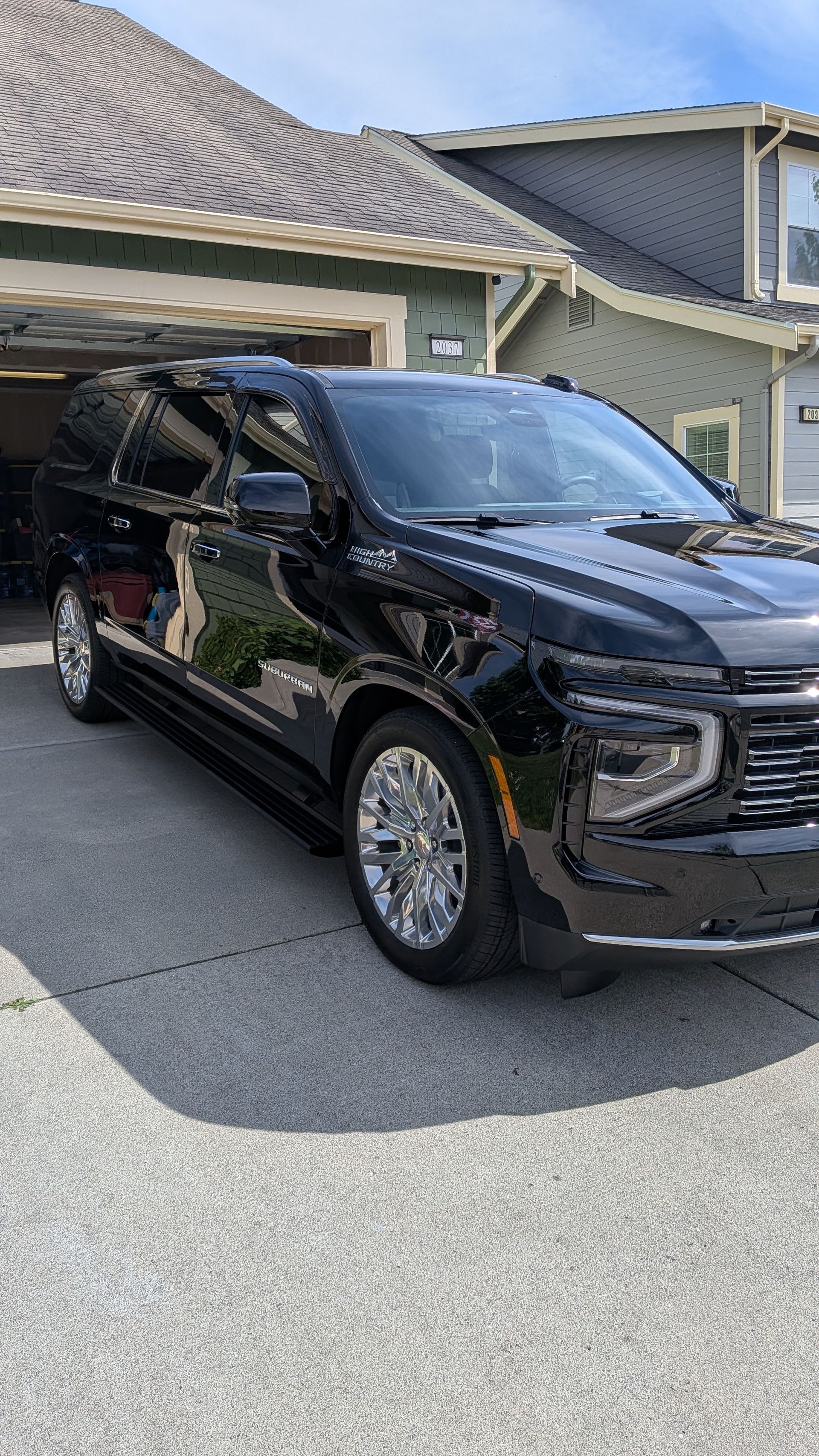 Black SUV parked in a driveway beside a house with gray siding and a shingled roof.