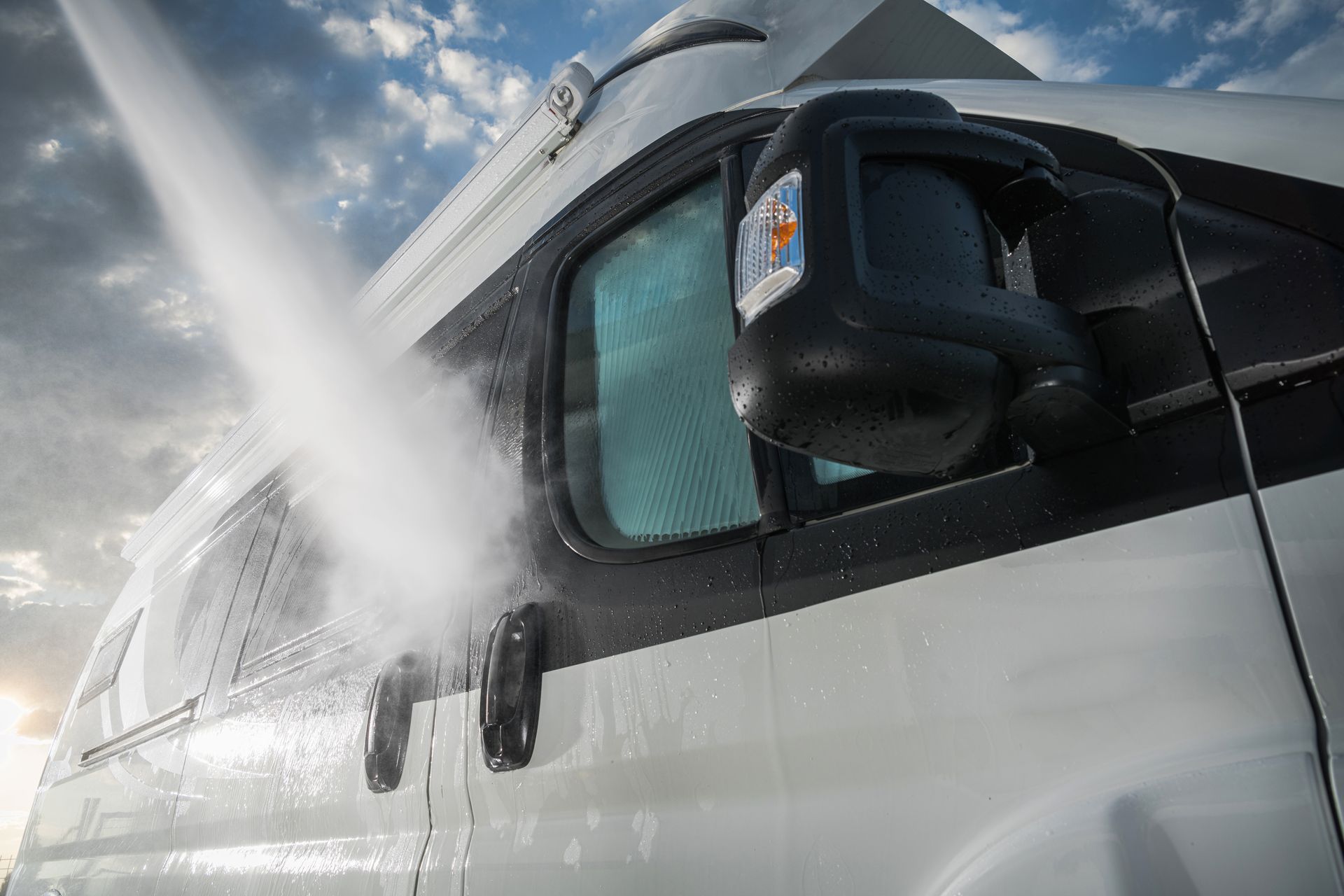 White van being washed with a strong stream of water against a cloudy sky