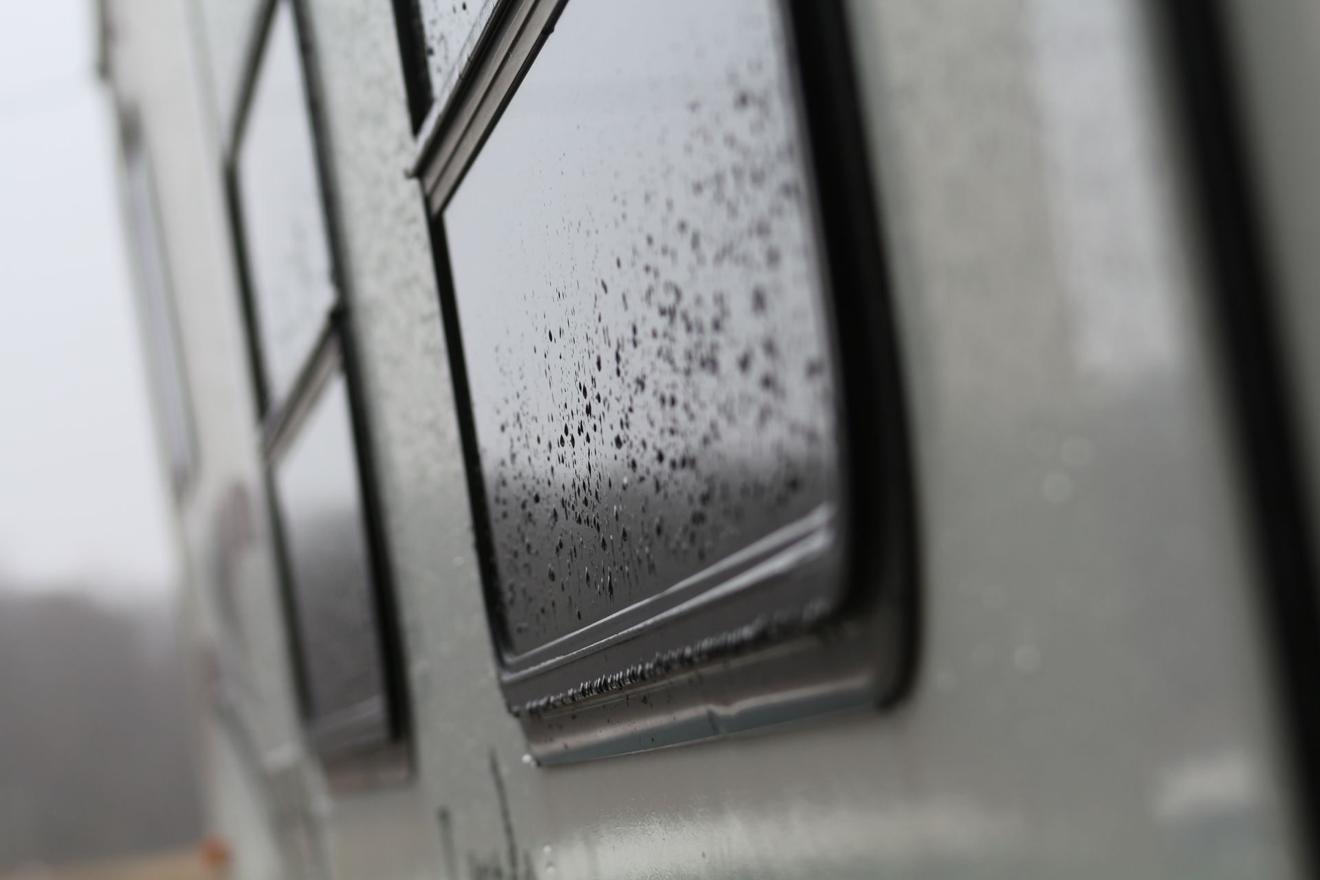Rain-speckled caravan windows on a gray vehicle exterior