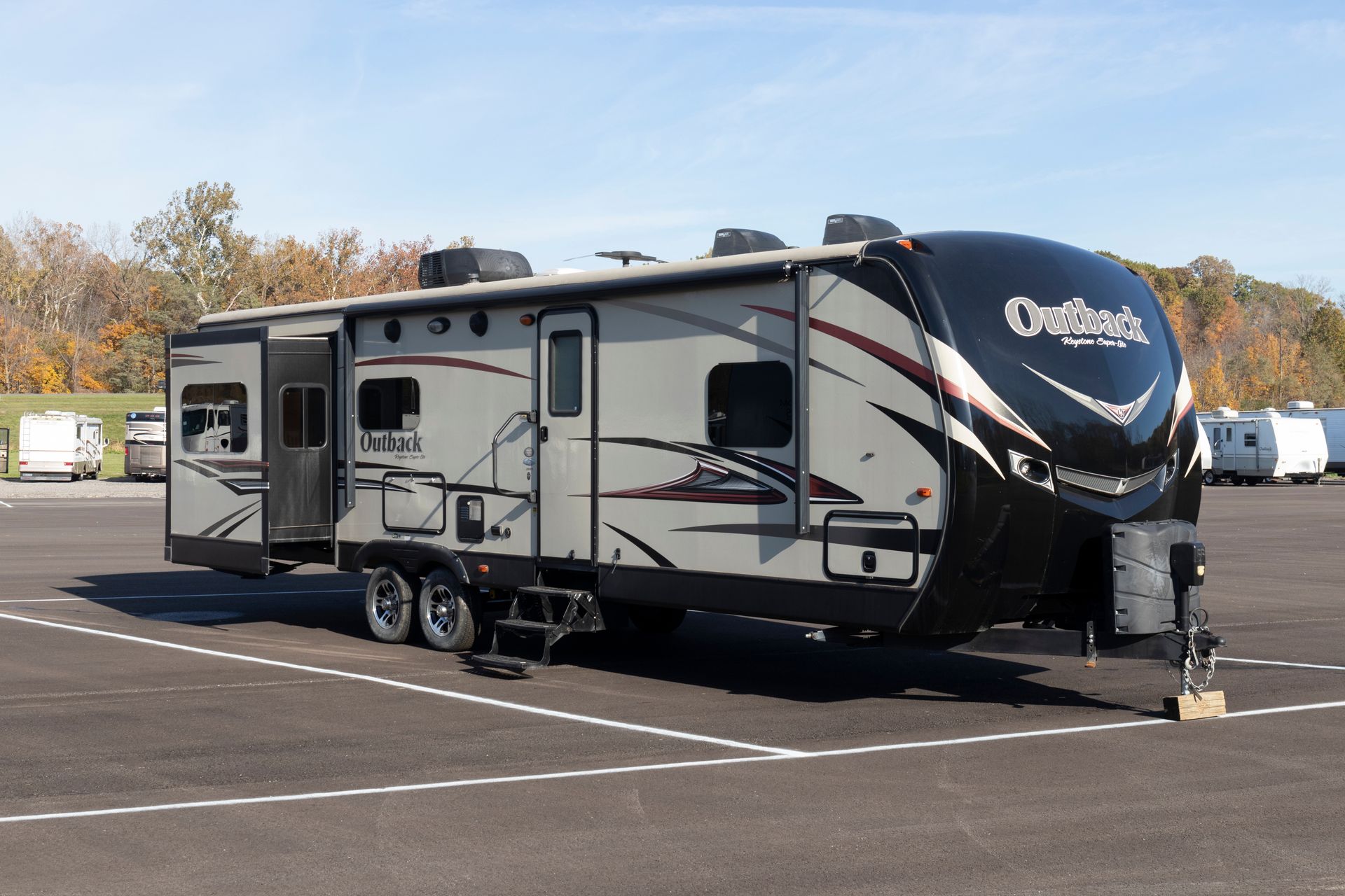 A tan and black travel trailer parked in a lot on a sunny day.